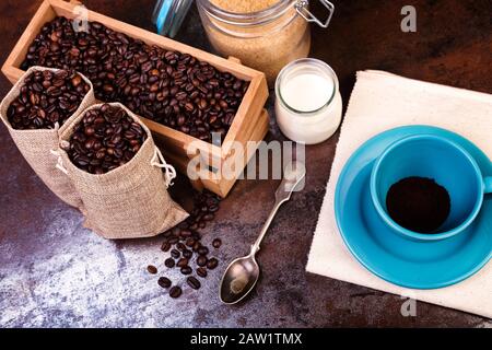 Tasse de sachets de café et de jute, récipients en bois remplis de fèves de cofée sur le fond de rouille. Sucre de canne. Faible luminosité. Banque D'Images