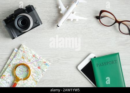 Vue du dessus des accessoires de voyage sur fond en bois. Appareil photo vintage plat, modèle d'avion, lunettes, carte avec loupe, smartphone et pastipo Banque D'Images