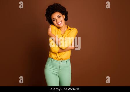 Photo de belle jolie peau sombre dame tenant les épaules profiter de sa propre entreprise privée s'aimer porter chemise jaune vert pantalon isolé couleur marron Banque D'Images