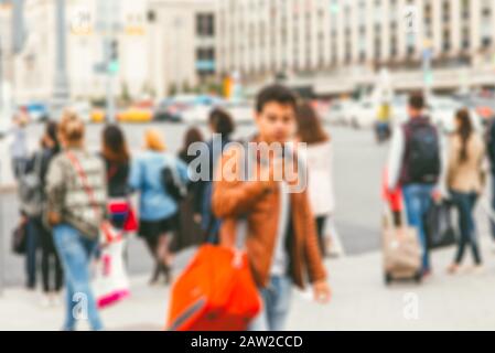 Un homme indéfini dans une veste en cuir marron avec un sac de randonnée rouge se tient à un passage à niveau. Arrière-plan flou de la ville Banque D'Images