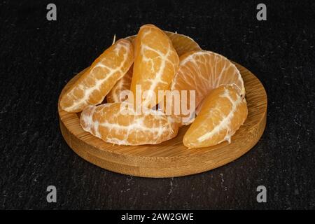 Groupe de sept morceaux de mandarine orange frais sur les montagnes russes rondes en bambou sur la pierre grise Banque D'Images