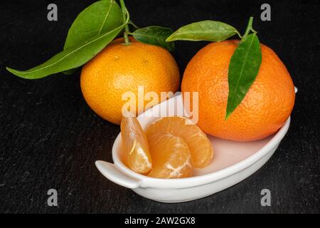 Groupe de deux trois morceaux de mandarine orange frais sur plaque en céramique blanche sur pierre grise Banque D'Images