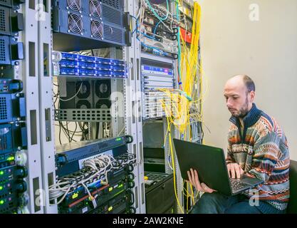 Un homme avec un ordinateur portable se trouve dans la salle serveur du centre de données. L'administrateur système travaille près des racks avec les serveurs. Ingénieur Informatique Banque D'Images