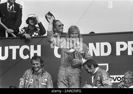 Nederlands: Huldiging van winnaar James Hunt, liens Niki Lauda. Le gagnant de la course, James Hunt, de Hesketh, se tient sur la première étape du podium au Grand Prix néerlandais de 1975. Flanquer de lui sont la Ferrari pair Niki Lauda (à gauche) et Clay Regazzoni (à droite), qui ont terminé respectivement en deuxième et troisième places; Banque D'Images