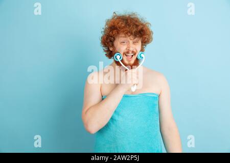 Portrait du jeune homme caucasien dans sa journée de beauté et la routine de soins de la peau. Modèle masculin avec poils rouges naturels massant le faceskin avec rouleau en pierre. Soins du corps et du visage, concept de beauté naturelle et masculine. Banque D'Images