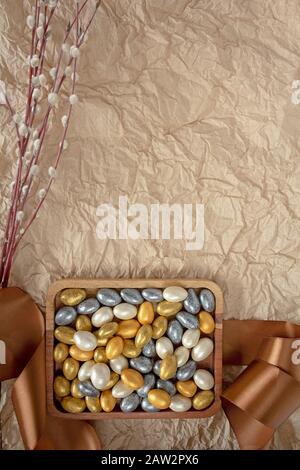 Un cadeau de Pâques joliment décoré dans une assiette en bois avec un ruban cadeau avec des branches de palmier sur un fond de papier artisanal à la menthe avec espace pour les copies Banque D'Images
