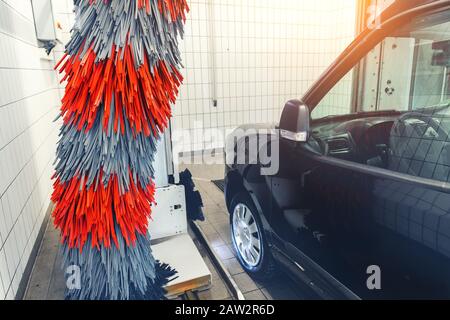 Mini-fourgonnette de livraison moderne noire avec machine de lavage automatique de voiture à tunnel robot. Brosses souples grises et rouges pour laver le véhicule avec de la mousse au gaz Banque D'Images