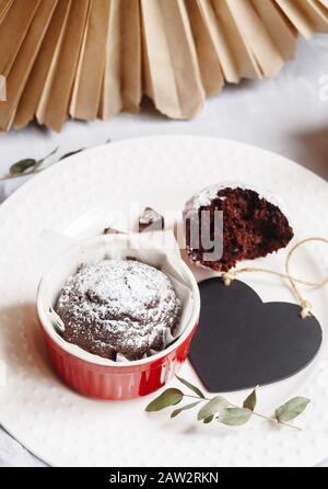 Muffin au chocolat dans une tasse rouge. Maquette valentine noir coeur copyspace. Petite ramekin en céramique vitré avec gâteau brun sur fond blanc Banque D'Images