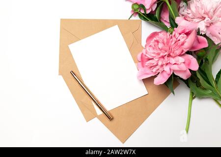 Carte de vœux à enveloppe d'artisanat, stylo doré avec bouquet de pivoines roses sur fond rose pour l'anniversaire, la fête des mères ou la Saint Valentin Banque D'Images