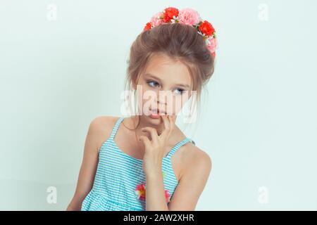 Belle petite fille couronne de fleurs sur la tête posant en studio main sur le menton près de la bouche. Gros plan portrait du modèle caucasien pour enfant avec bandeau floral Banque D'Images