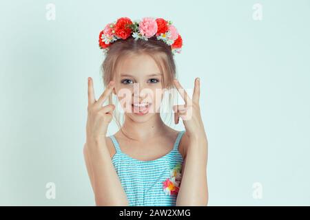 Fille d'enfant montrant le signe de victoire avec les doigts regardant votre appareil photo heureux. Gros portrait du modèle caucasien pour enfant avec bandeau floral sur la tête, isolé Banque D'Images