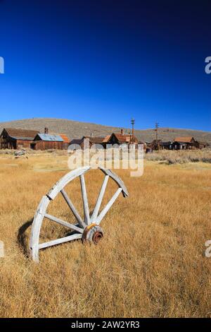 Ancienne roue en bois posée seul dans l'herbe sèche près de la ville fantôme abandonnée, ville minière d'or Bodie en Californie. ÉTATS-UNIS Banque D'Images