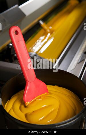 Spatulaire rouge dans un pot de peinture jaune pour l'industrie de l'impression Banque D'Images