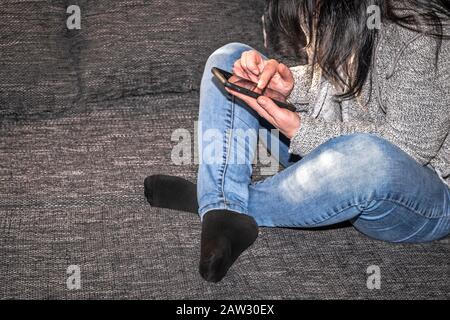 Une fille avec des cheveux noirs est assise sur un lit tenant un téléphone dans sa main Banque D'Images