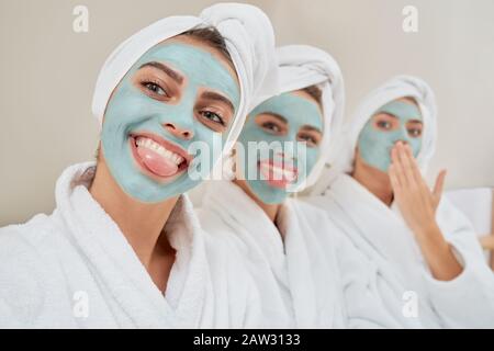 Gros plan sur un groupe souriant de filles avec masques cosmétiques, serviettes sur la tête et peignoirs prenant le selfie après la douche dans la chambre. Trois filles émotionnelles s'amuser. Concept d'amitié, de soins de la peau. Banque D'Images