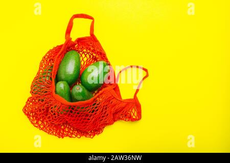 Avocats fruits dans un sac écologique en mesh rouge réutilisable. Sac en mesh recyclé pour fruits ou légumes. Concept d'achat sans plastique, zéro déchet. Pose plate minimale Banque D'Images