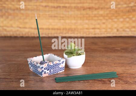 Composition avec des bâtons d'encens se trouvent sur une table en bois et un bâton brûle dans un stand traditionnel ornemental, plante verte fraîche dans la casserole. Ince parfumé Banque D'Images