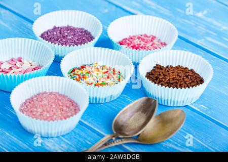 Des bonbons colorés saupoudrer sur le porte-cupcake en papier. Fond rustique en bois bleu et cuillère argentée. Banque D'Images