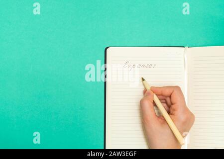 Directement au-dessus de la vue de la main de femme tenant la plume écriture des dépenses dans un bloc-notes sur fond vert. Vue de dessus, espace de copie. Banque D'Images