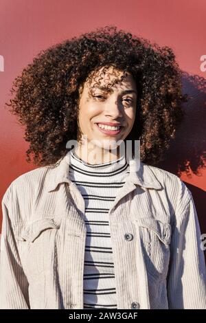 portrait vertical d'une belle latina souriante avec des cheveux bouclés d'afro sur un fond rouge, concept de beauté et de diversité Banque D'Images