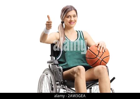 Jeune femme dans un fauteuil roulant tenant le basket-ball et montrant des pouces vers le haut isolé sur fond blanc Banque D'Images