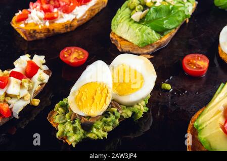 Toasts de patate douce avec avocat, œufs durs, tomates et graines de sésame sur fond sombre. Concept de repas sain. Cuisine propre, plats du Pescetarian, vue sur le dessus Banque D'Images