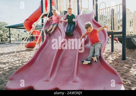 Actif heureux caucasiens enfants glissants sur cour de l'école extérieure de terrain de jeu le jour ensoleillé d'été. Enfants amis garçons fille s'amuser. Activité saisonnière pour les enfants Banque D'Images