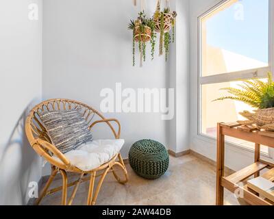 Intérieur de la chambre avec chaise en rotin avec coussin, plantes suspendues macrame et pouf en fibre dans un salon avec une grande fenêtre. Détendez-vous dans la salle de retraite. Hy Banque D'Images