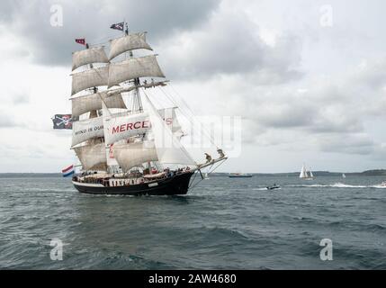 L'immense bateau à cinq gouttes navigué, à deux mâts, la Mercedes volant le Jolly Roger, Skull et les croisillons drapeau dans une brise raide au large de Falmouth. Banque D'Images