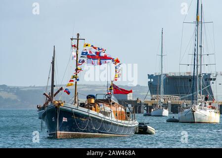 Bateau de sauvetage RNLI de style ancien au soleil éclatant au point d'ancrage vêtu d'un ensemble de drapeaux colorés et de pennants sur fond de yachts et de cuirassé Banque D'Images