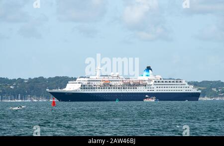 Immense paquebot de croisière Saga dans les eaux du port de Falmouth avec de petits bateaux et fond de terre pour illustrer son énorme échelle. Banque D'Images