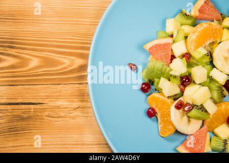 Salade de fruits frais sur une plaque bleue qui se tient sur une table en bois avec un endroit pour l'inscription. Salade d'agrumes avec espace publicitaire Banque D'Images