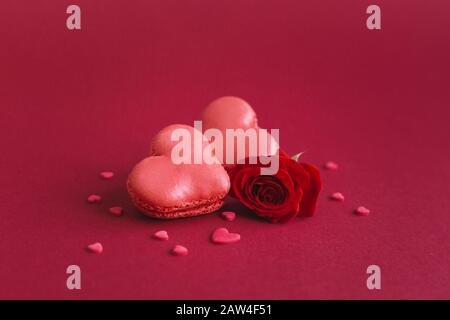 Macarons en forme de coeur avec rose rouge sur fond rouge foncé, décoré de coeurs doux. Concept pour la Saint Valentin. Placer pour le texte. Banque D'Images