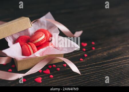 Macarons français rouges dans une boîte décorée de coeurs doux et de ruban sur une table en bois sombre. Concept pour la Saint-Valentin. Placer pour le texte. Banque D'Images