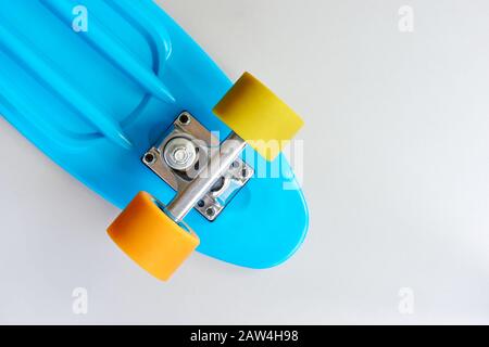 Détail de mini-pension ou de planche à roulettes en plastique bleu avec roues jaune et orange et fixation en métal sur fond gris clair. Banque D'Images