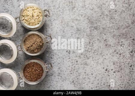 Graines de chanvre, graines de lin brunes et graines de lin dans un bocal en verre sur une table grise. Vue de dessus. Espace pour le texte. Santé et détox. Manger propre. Perte de poids. Banque D'Images