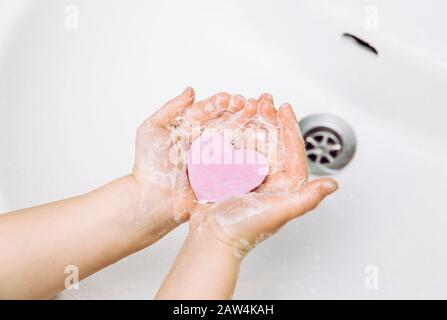 Importance des soins d'hygiène personnelle. Vue plate sur la couche de savon pour enfants se lavant les mains sales avec une barre de savon rose en forme de coeur, beaucoup de mousse. Espace de copie. Banque D'Images