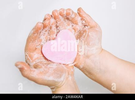 Importance des soins d'hygiène personnelle. Vue plate sur la couche de savon pour enfants se lavant les mains sales avec une barre de savon rose en forme de coeur, beaucoup de mousse. Espace de copie. Banque D'Images