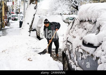 Vieil homme, homme en hiver, nettoyage des manteaux, allée de pelles, rue de la neige couverte avec pelle, maisons résidentielles, voitures garées sur la route dans Bu Banque D'Images