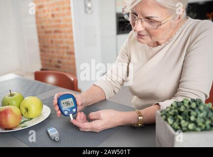 Senior woman with glucomètre contrôler le niveau de sucre dans le sang à la maison. Le diabète, concept de soins de santé Banque D'Images