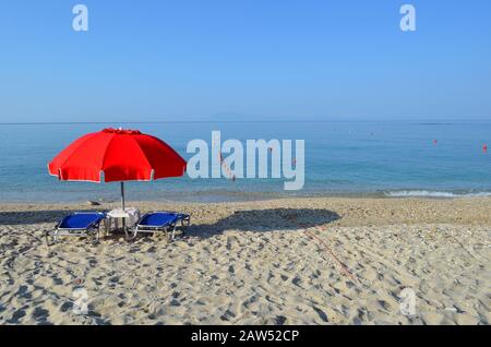 Parasol rouge et deux chaises longues sur une plage de sable vide Banque D'Images
