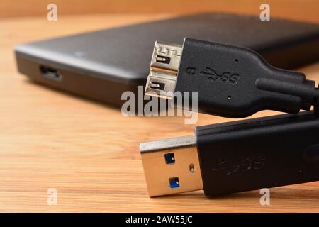 Prise de vue macro du câble USB 3.0 en premier plan et disque dur USB 3.0 externe en arrière-plan, noir et plat, sur base en bois Banque D'Images