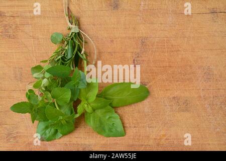 Plantes aromatiques vertes fraîches, basilic, romarin, menthe poivrée, menthe mojito et origan attachés dans un bouquet sur fond de bois Banque D'Images