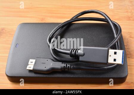 Disque dur USB 3.0 externe noir et plat avec câble USB 3.0 enroulé sur fond en bois, vue latérale Banque D'Images