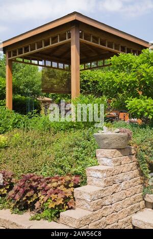 Bordure en pierre surélevée avec Heuchera - fleurs de corail et belvédère en bois brun dans jardin privé arrière-cour à la fin du printemps. Banque D'Images
