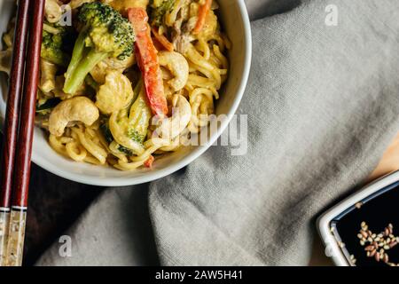 Gros plan de nouilles au curry jaune thaï avec noix de cajou et légumes dans un bol Banque D'Images