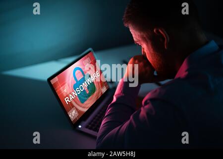 Inquiets Businessman Looking At Laptop avec Ransomware mots à l'écran sur le lieu de travail Banque D'Images