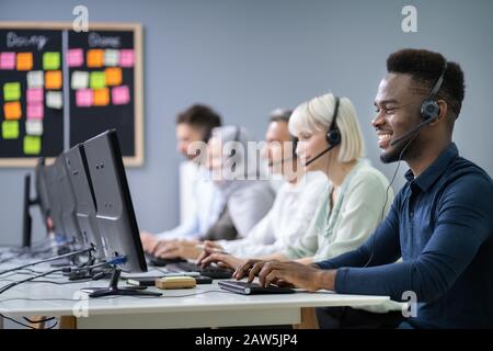 L'agent des services à la clientèle masculine positive avec casque de travail dans un centre d'appels Banque D'Images