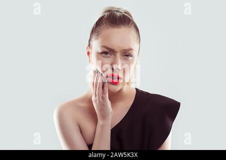 Mal aux dents. Jeune femme avec le problème sensible de la couronne de mal de dents sur le point de pleurer de la douleur touchant à l'extérieur de la bouche avec main isolé blanc léger bleu dos Banque D'Images