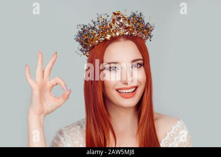Bonne femme donnant le signe ok. Bonne fille. Jolie femme avec couronne de cristal sur la tête isolée sur un mur vert clair de fond gris. Humain positif Banque D'Images